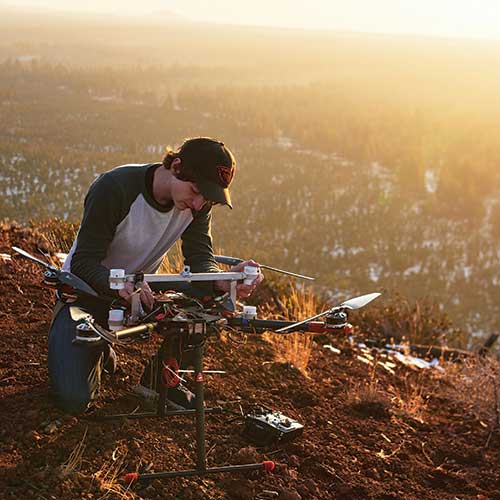 person inspecting a drone on top of a mountain
