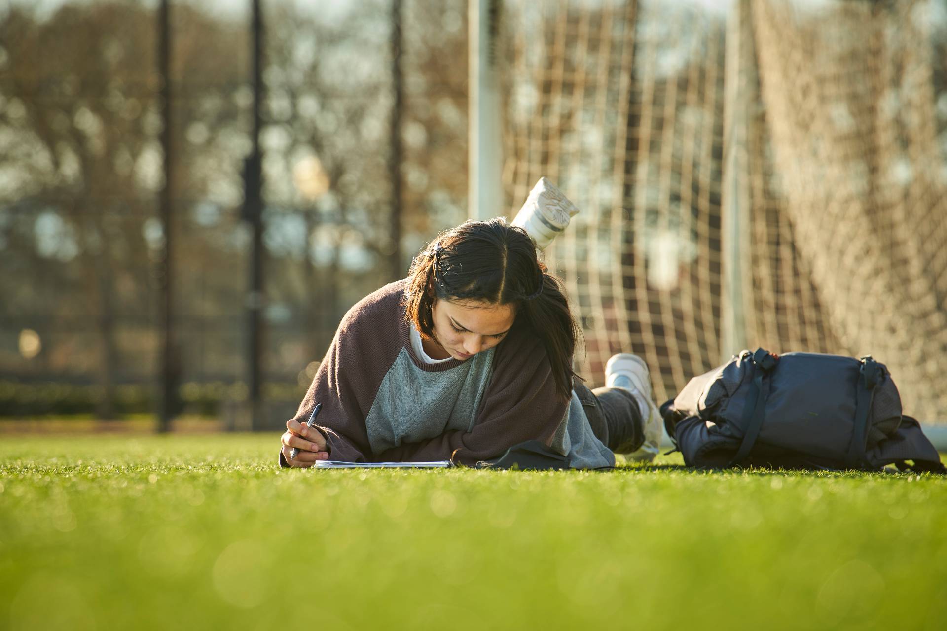 person lying on grass, writing in a notebook