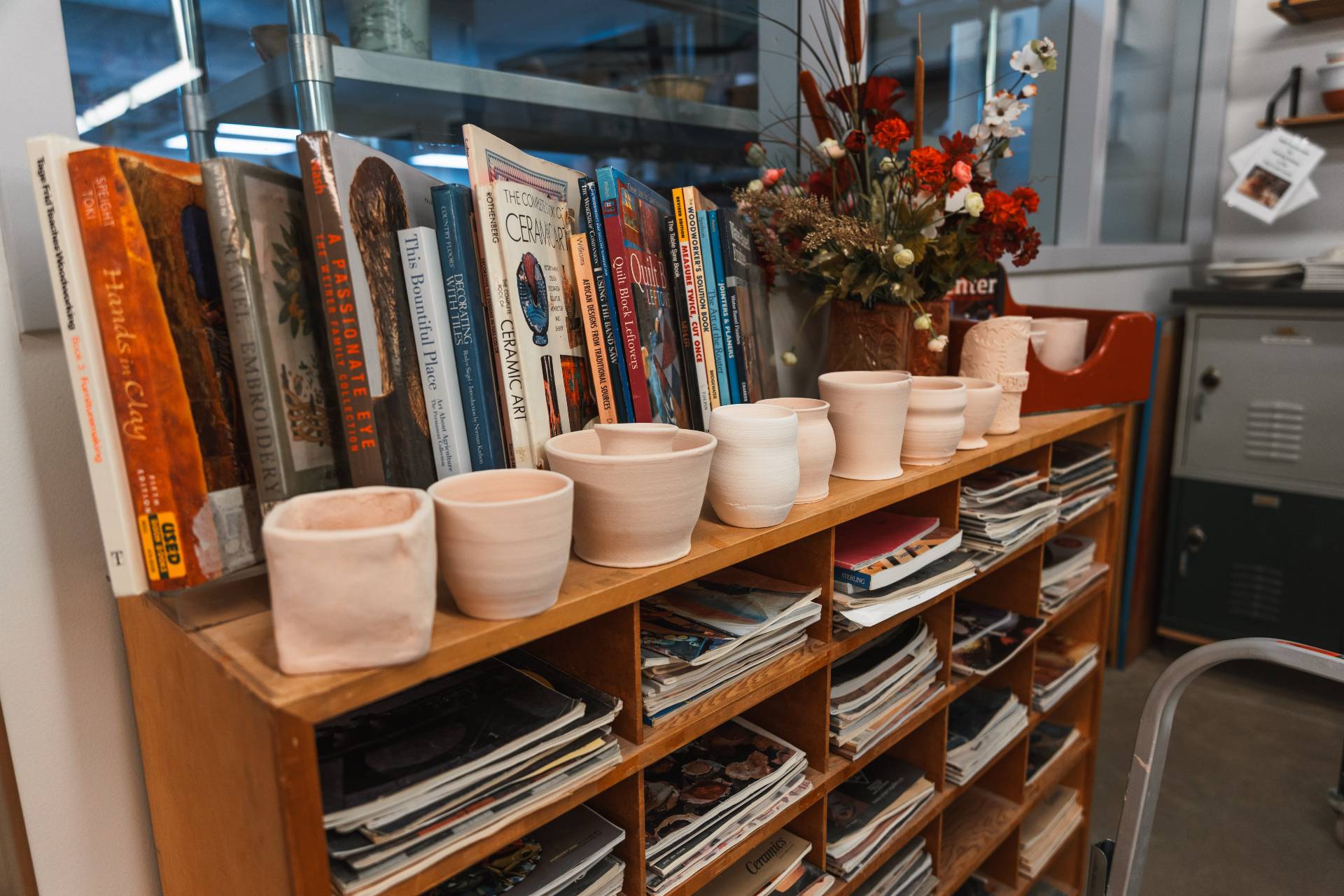 bookshelf filled with magazines, with a row of unglazed pottery on top