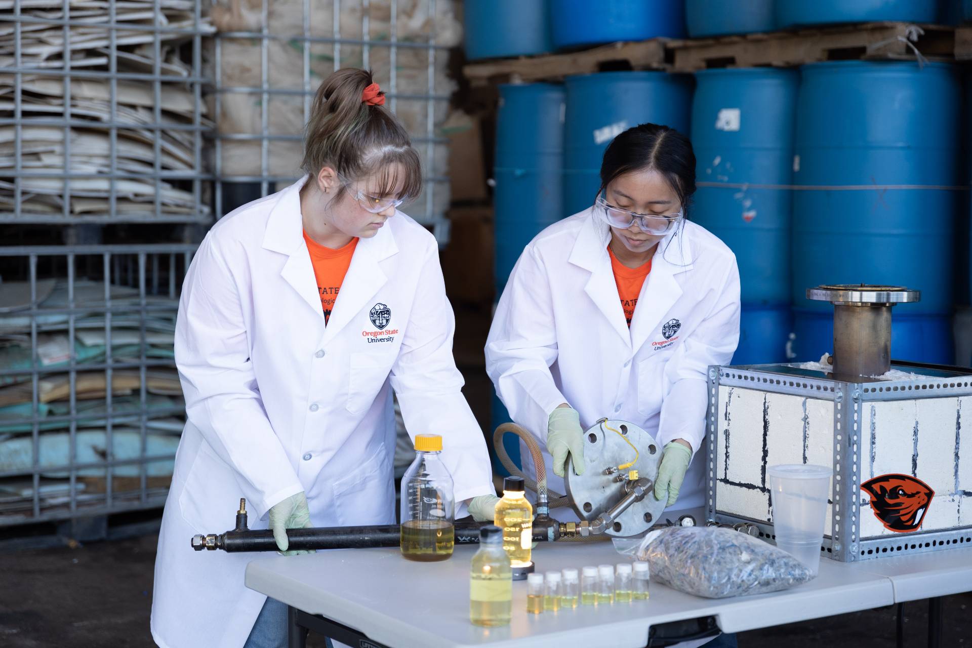 two researchers in a lab coats load plastic into kiln reactor