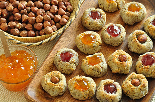 hazelnuts next to tray of hazelnut cookies with a jar of jam