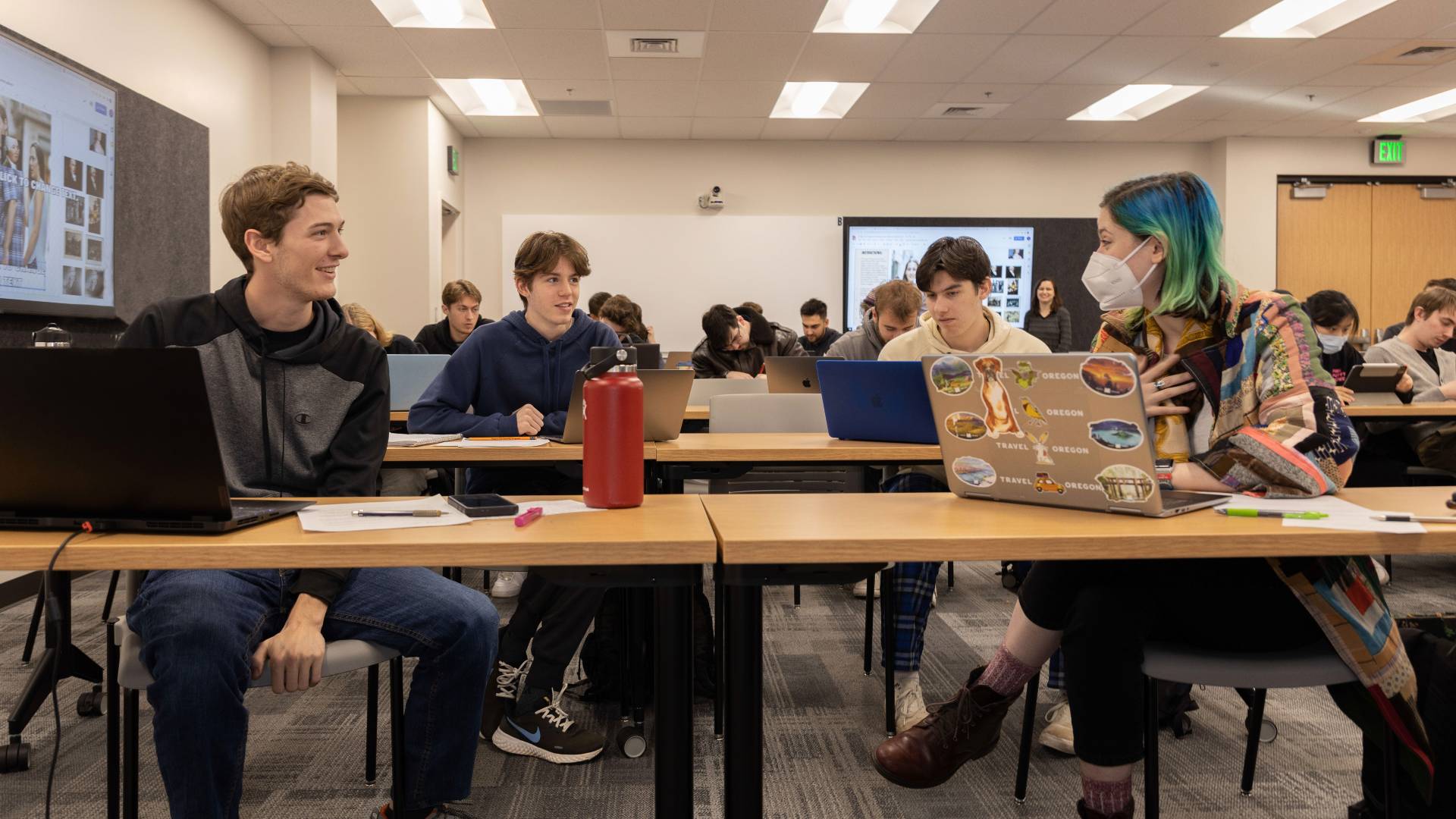 students discussing with laptops at wood tables 