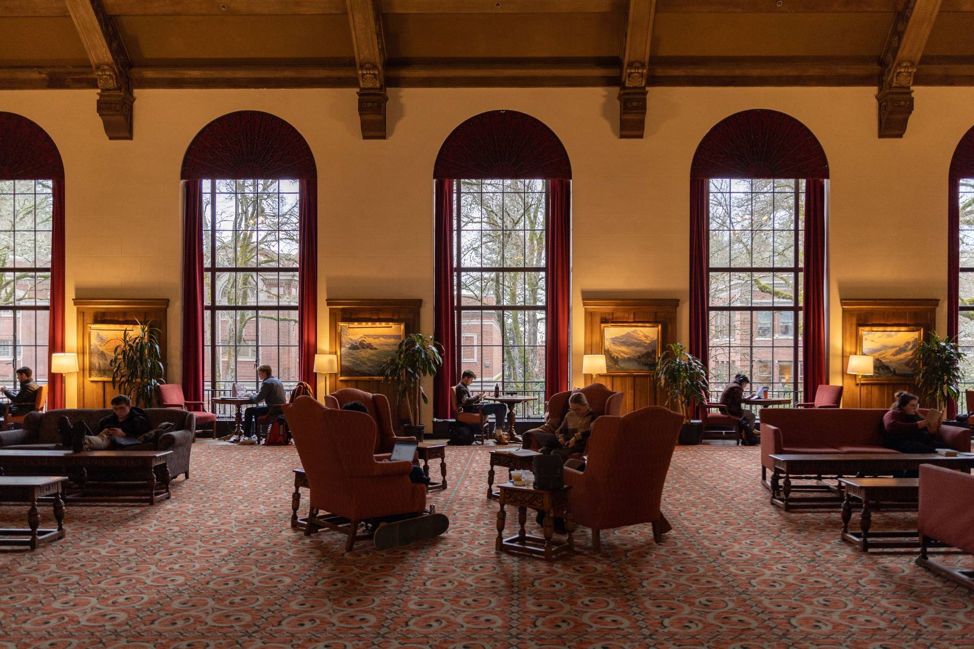 people in high backed chairs in the Memorial Union lounge which features high windows, a large rug and sofas