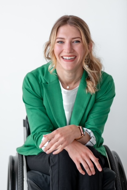 Lizzy Ragan in a green blazer and black pants sitting in a wheelchair
