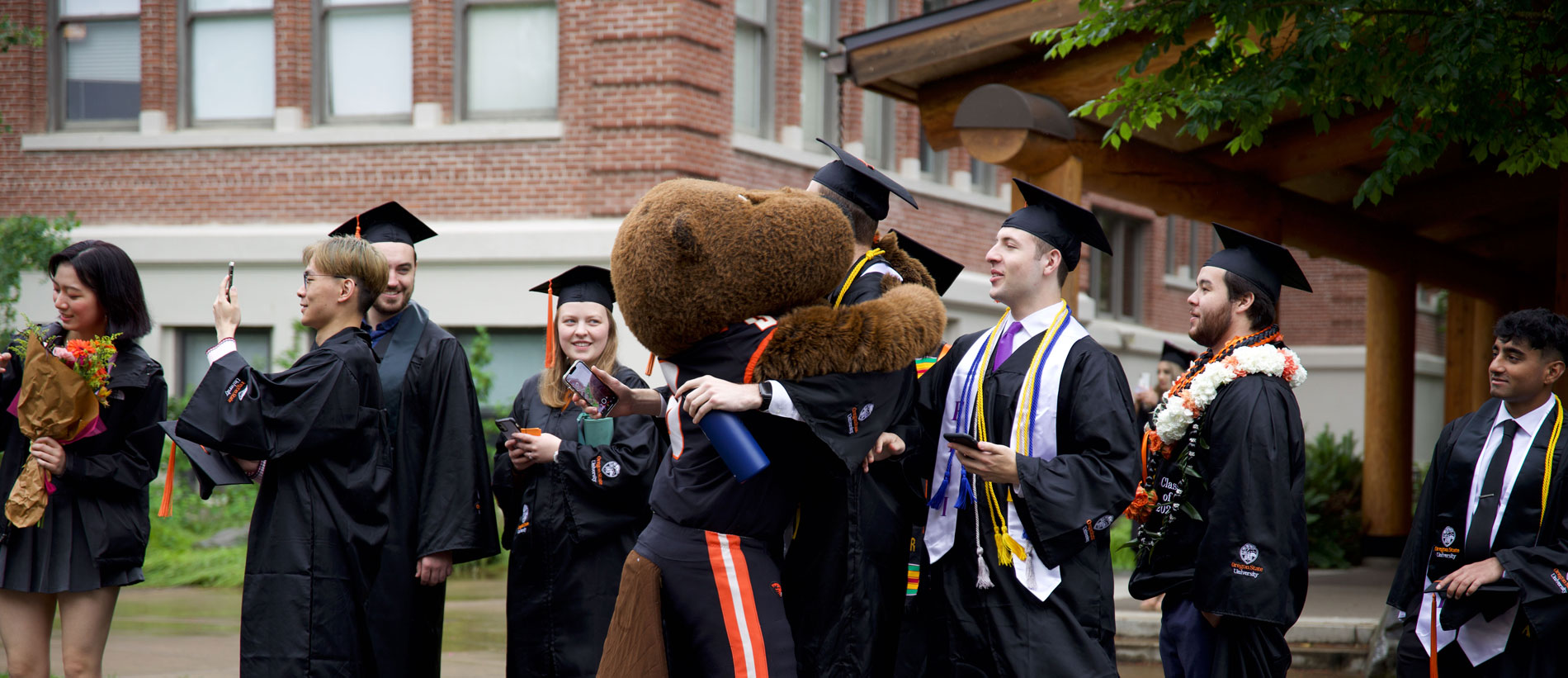 Benny Beaver hugging a graduate surrounded by others in caps and gowns