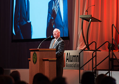 Ed Ray stands a podium with the sign that read "Alumni Association" in the background