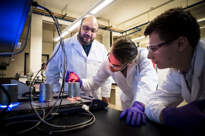 3 people in white lab coats inspecting a vial in red light