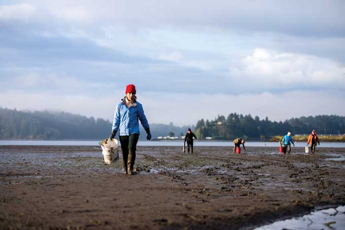 person in red hat and  blue jacket walking with a bucket on a seaweed covered beach