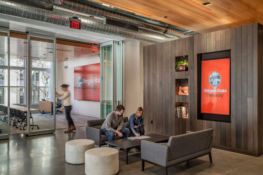 people sitting in a lobby with a large screen with the Oregon State University logo