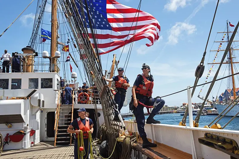Steenson standing on the edge of a large ship with an American flag waving above her with two crewmates standing next to her
