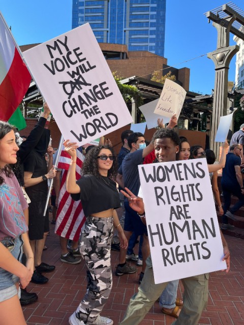 Moallem at a protest holding a sign that says "My Voice Will Change the World"