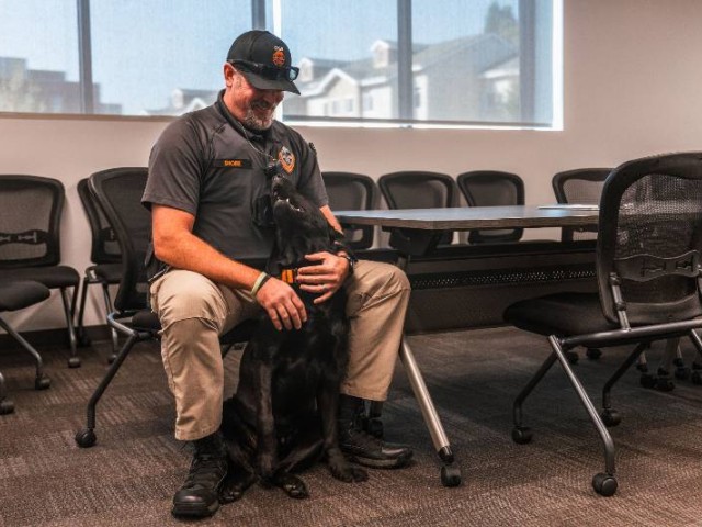 Cedar the dog sitting at a police officer's feet, looking up at him