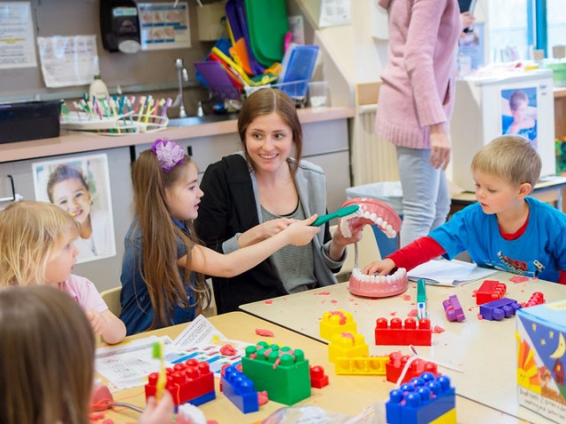 teaching assistant sitting at table with children while playing with building blocks